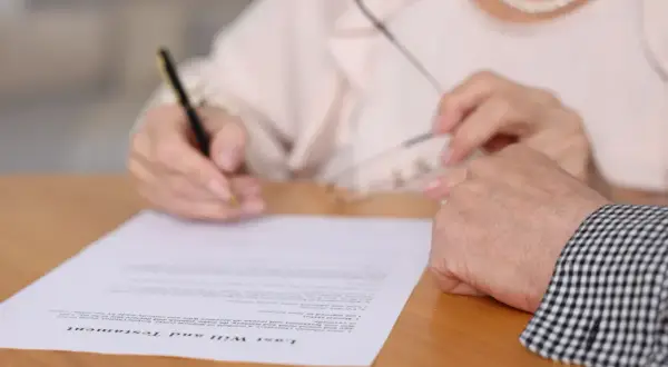 Kto ma wgląd do testamentu? Dłoń podpisuje dokument "Last Will and Testament", a obok spoczywa druga dłoń.