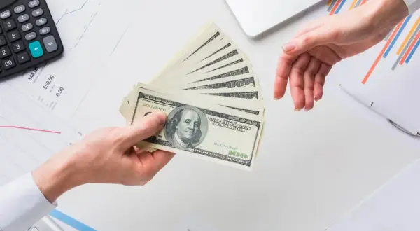 Przekazanie pieniędzy na rachunek bankowy. Dłonie przekazują stos banknotów 100 dolarowych.