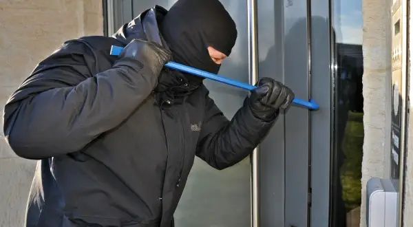 Mężczyzna w kominiarce i rękawiczkach próbuje wyważyć drzwi łomem. To próba kradzieży z włamaniem.
