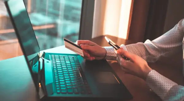 Kobieta z kartą kredytową i telefonem przy laptopie. Zastanawia się, czy trzeba zwrócić błędny przelew.