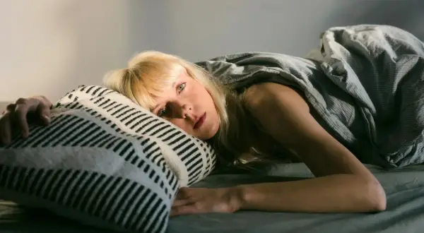 Kobieta leży w łóżku, przytulając poduszkę. Może to być obraz symbolizujący potrzebę urlopu menstruacyjnego w Polsce.