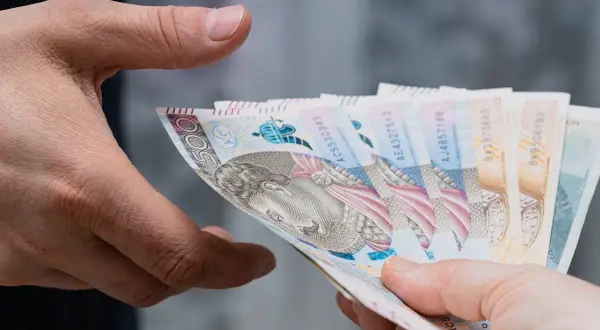 Dwie dłonie przekazują sobie plik banknotów. Zastanawiasz się, ile bank zabiera po śmierci?
