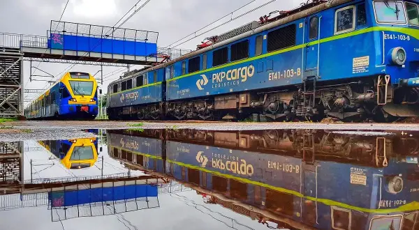 Dwa pociągi PKP, towarowy i pasażerski, odbijają się w kałuży. Po śmierci akcje pracownicze PKP budzą nadzieję na lepszą przyszłość.