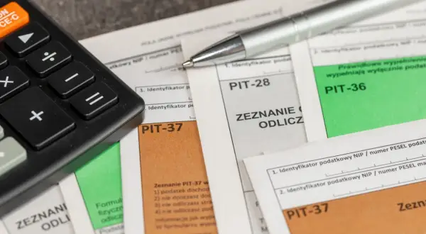 Kalkulator i długopis leżą na dokumentach PIT-37, PIT-28 i PIT-36. Czas na rozliczenie podatku i skorzystanie z ulg, czyli ikze odliczenie od podatku.