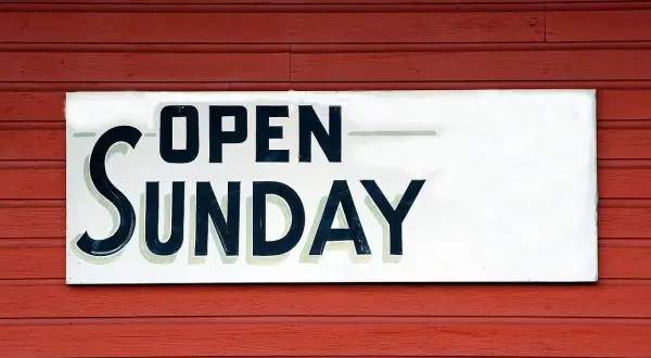 Tablica "OPEN SUNDAY" na czerwonej, drewnianej ścianie. To znak, że praca w niedziele jest możliwa.