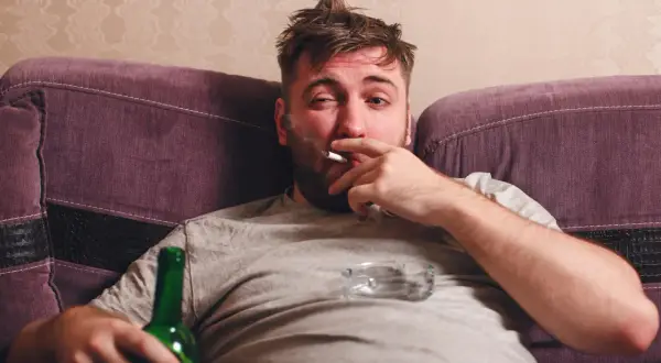 Mężczyzna z papierosem i butelką piwa na kanapie. Ciężki obowiązek alimentacyjny wobec brata alkoholika.