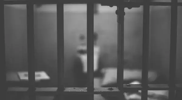 Widok przez kraty więzienne. Rozmazana postać w tle sugeruje nadzieję na odroczenie kary pozbawienia wolności.