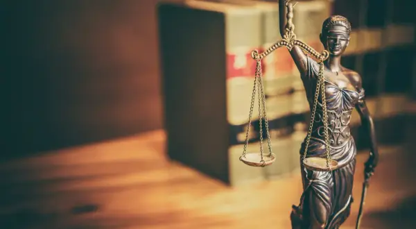 Figurka Temidy z wagą symbolizuje sprawiedliwość. W tle widać regały z książkami, sugerujące prawniczy kontekst, jak wniosek o wstrzymanie wykonania kary do czasu rozpatrzenia wniosku wzór.