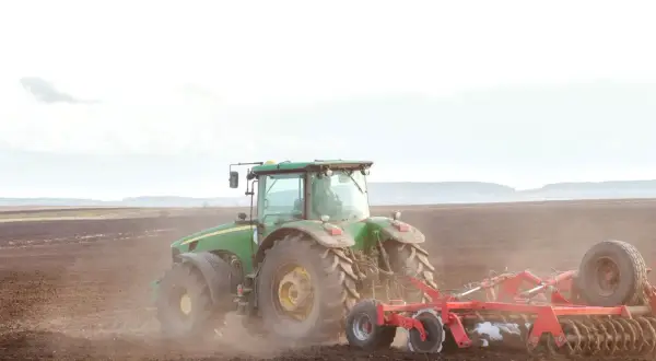 Zielony traktor orze pole. To obraz przyszłości, gdzie przekazanie gospodarstwa rolnego idzie w parze z opieką nad rodzicami, zapewniając stabilność i ciągłość.