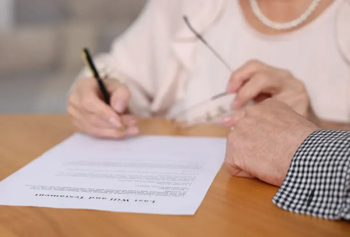 Kto ma wgląd do testamentu? Dłoń podpisuje dokument "Last Will and Testament", a obok spoczywa druga dłoń.