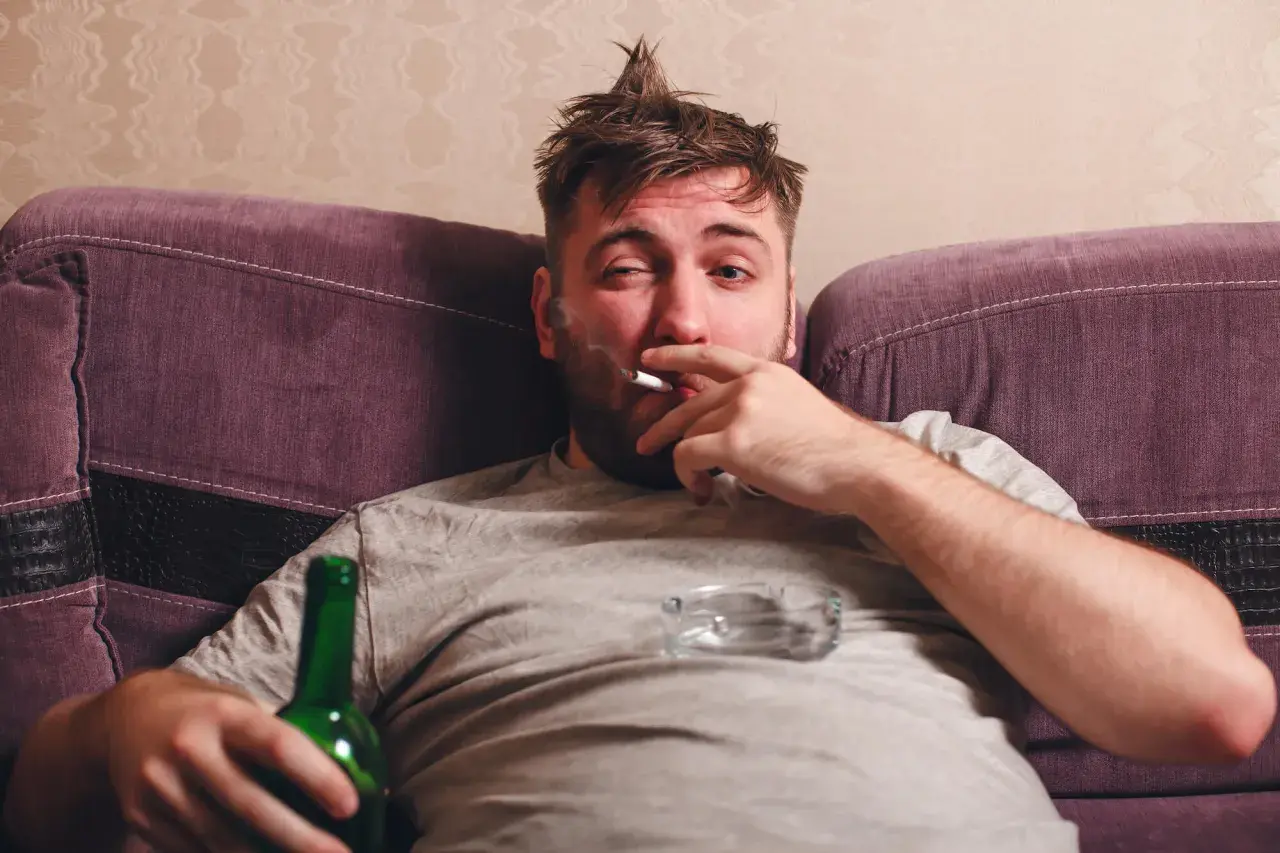 Mężczyzna z papierosem i butelką piwa na kanapie. Ciężki obowiązek alimentacyjny wobec brata alkoholika.
