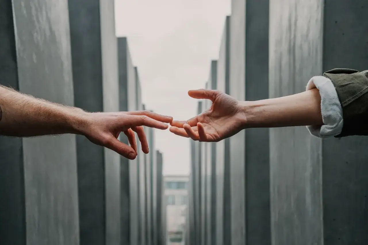 Dwie dłonie zbliżają się do siebie, symbolizując nadzieję na ponowne spotkanie. To jak dodatek za rozłąkę, który sprawia, że każdy gest jest ważniejszy.