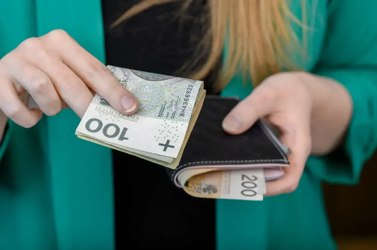 Ręce wkładają banknoty 100 zł do portfela, w którym są już 200 zł. To symboliczny gest wsparcia, gdy trwa obowiązek alimentacyjny wobec brata alkoholika.