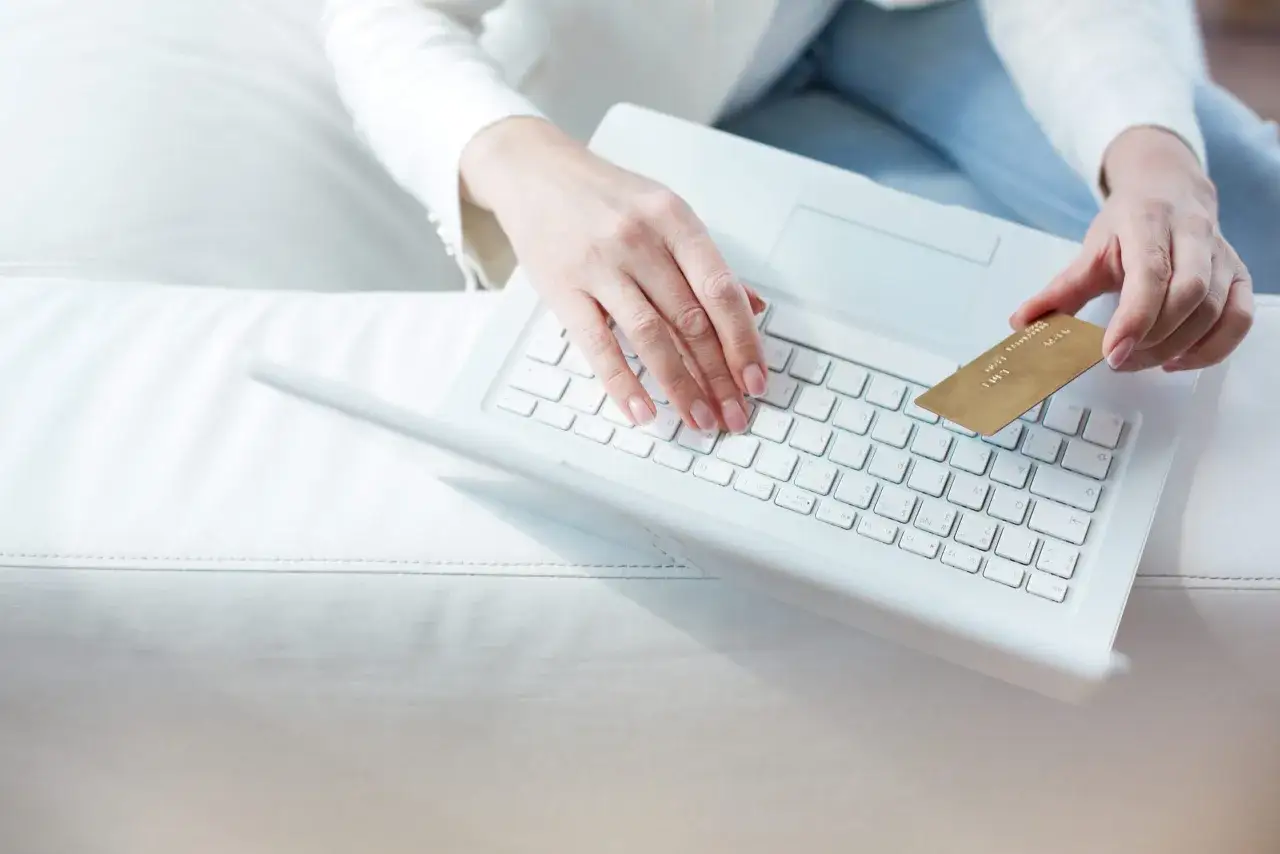 Kobieta z kartą płatniczą wpisuje dane na laptopie, zastanawiając się, czy trzeba zwrócić błędny przelew.