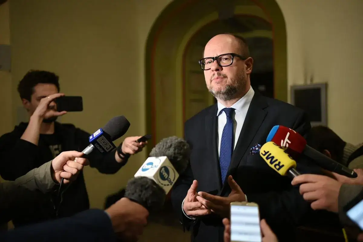 Mężczyzna w garniturze odpowiada na pytania dziennikarzy. Warto pamiętać, co grozi za naruszenie nietykalności cielesnej, by unikać takich sytuacji.