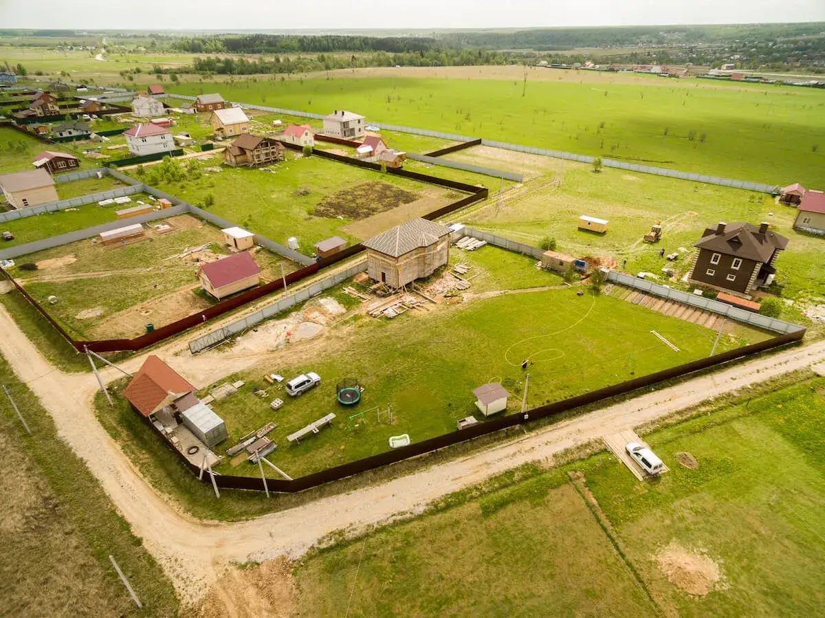 Osiedle domów w budowie, gdzie jedna działka jest już sprzedana, a inne czekają na zagospodarowanie. W tle pola i lasy.