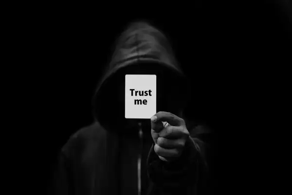 Postać w kapturze trzyma kartkę z napisem "Trust me". To symbol oszustwa, które może być karane z kodeksu karnego.