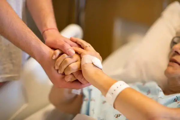 Dłoń opiekuna obejmuje dłoń osoby starszej w łóżku. Po śmierci osoby ubezwłasnowolnionej opiekun prawny ma obowiązki.