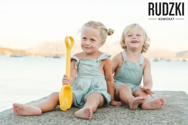 Dwie uśmiechnięte dziewczynki, przyrodnie rodzeństwo, bawią się na plaży z żółtą łopatką.