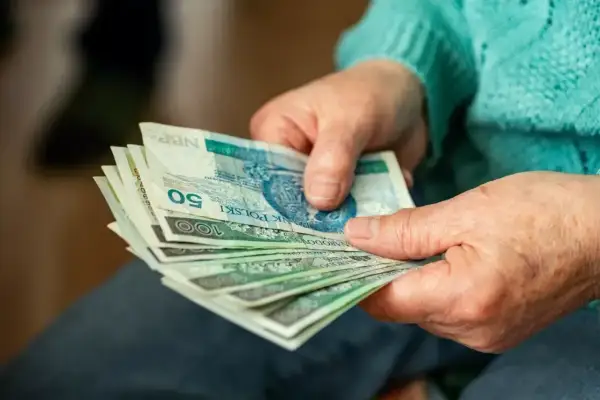 Dłonie trzymające polskie banknoty, być może jako dodatek za pracę w warunkach szkodliwych. Widoczne nominały 50 i 100 zł.