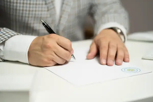 Mężczyzna w eleganckim garniturze pisze długopisem na białej kartce, przygotowując uzasadnienie pozwu o alimenty.