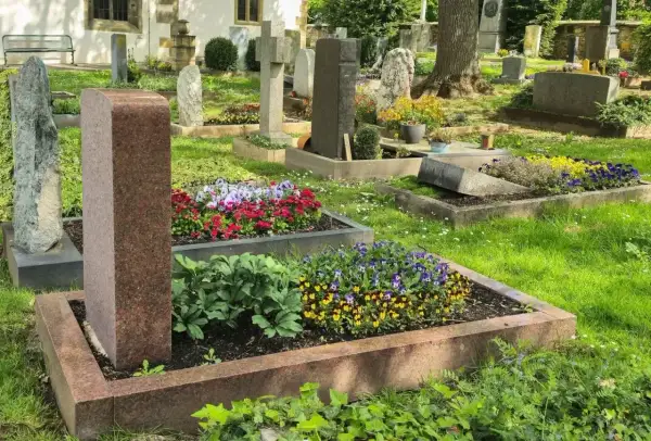 Cmentarz z zadbanymi nagrobkami i kwitnącymi kwiatami. Każdy grób to symbol prawa do grobu i pamięci.