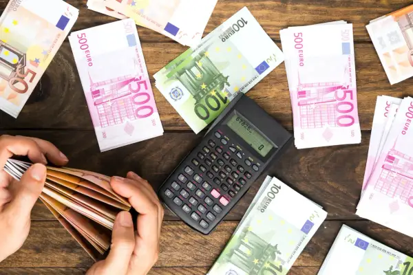 Ręce liczą banknoty euro. Obok kalkulator i stosy pieniędzy. Planowanie spadku dla obcej osoby i podatek od niego.