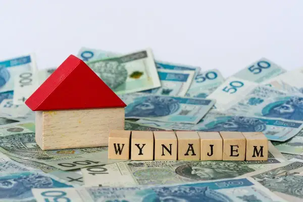 Drewniany domek i kostki z napisem "WYNAJEM" na tle polskich banknotów. Zastanawiasz się nad najmem okazjonalnym i podatkiem?