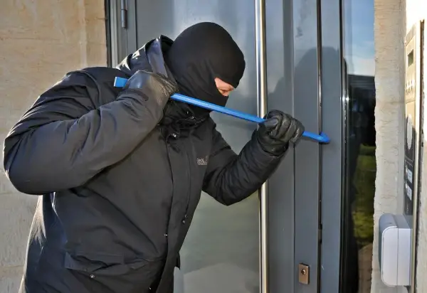 Mężczyzna w kominiarce i rękawiczkach próbuje wyważyć drzwi łomem. To próba kradzieży z włamaniem.