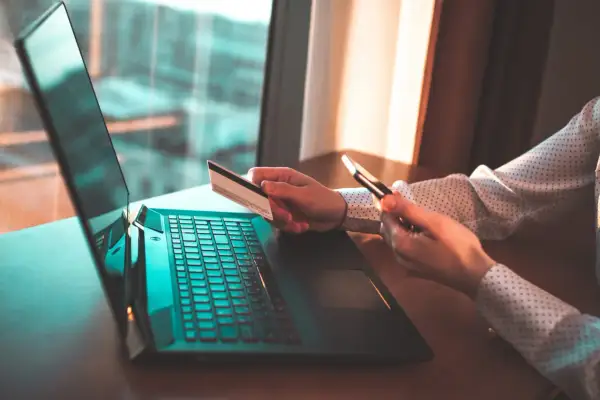 Kobieta z kartą kredytową i telefonem przy laptopie. Zastanawia się, czy trzeba zwrócić błędny przelew.