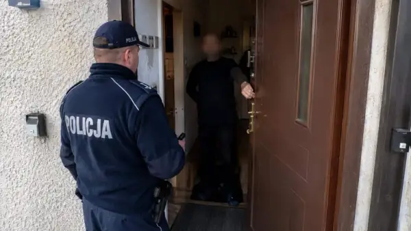 Policjant stoi przed drzwiami, gdzie mężczyzna otwiera wejście. Sytuacja może dotyczyć włamania bez kradzieży kodeks karny.