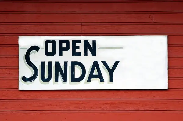 Tablica "OPEN SUNDAY" na czerwonej, drewnianej ścianie. To znak, że praca w niedziele jest możliwa.