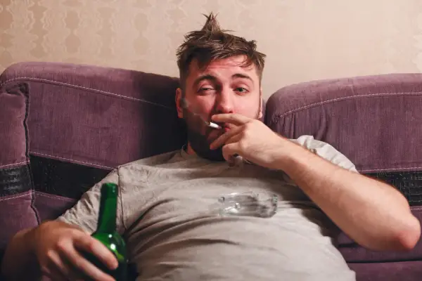 Mężczyzna z papierosem i butelką piwa na kanapie. Ciężki obowiązek alimentacyjny wobec brata alkoholika.