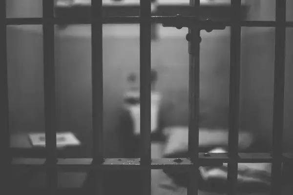 Widok przez kraty więzienne. Rozmazana postać w tle sugeruje nadzieję na odroczenie kary pozbawienia wolności.
