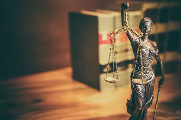 Figurka Temidy z wagą symbolizuje sprawiedliwość. W tle widać regały z książkami, sugerujące prawniczy kontekst, jak wniosek o wstrzymanie wykonania kary do czasu rozpatrzenia wniosku wzór.